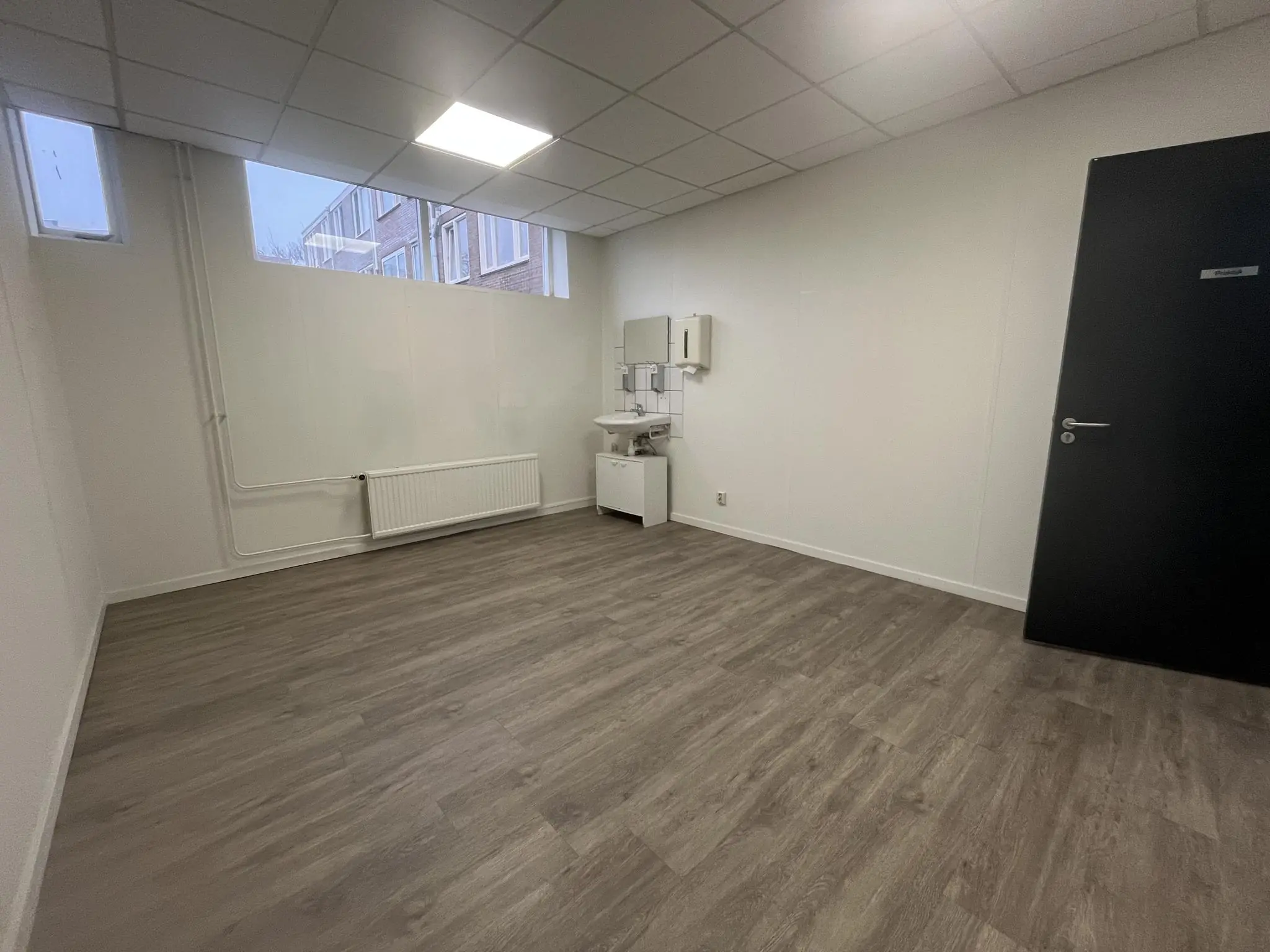 Lege kantoorruimte met wastafel aan de Burgemeester Smitsstraat, voorzien van laminaatvloer en systeemplafond.